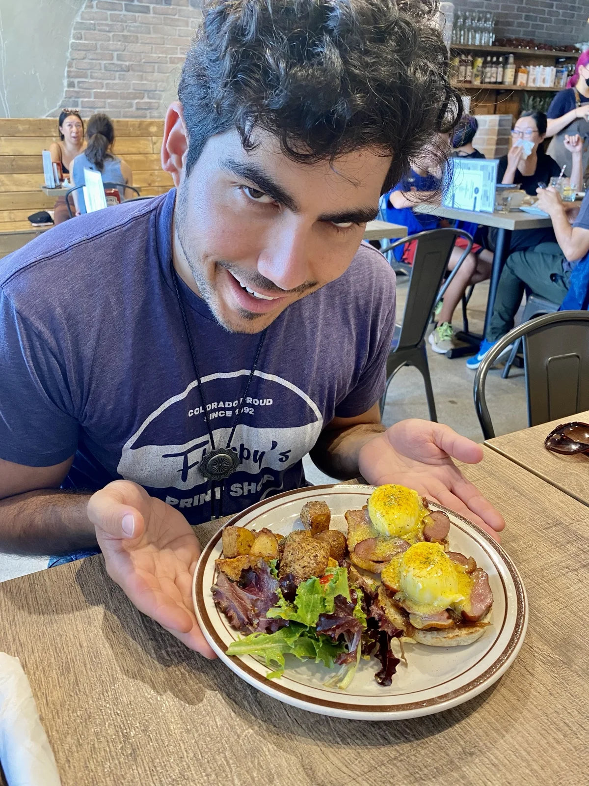 guy in Colorado tee presenting eggs benedict w/ hollandaise + roast potatoes + salad in…