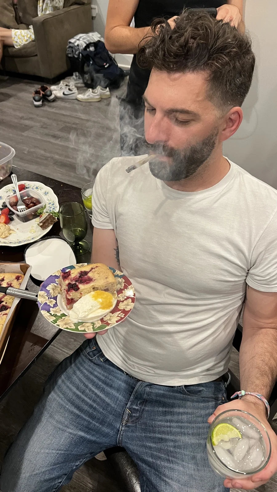 bearded guy in white tee holding plate of berry cobbler w/ ice cream, smoke/vape puff, …