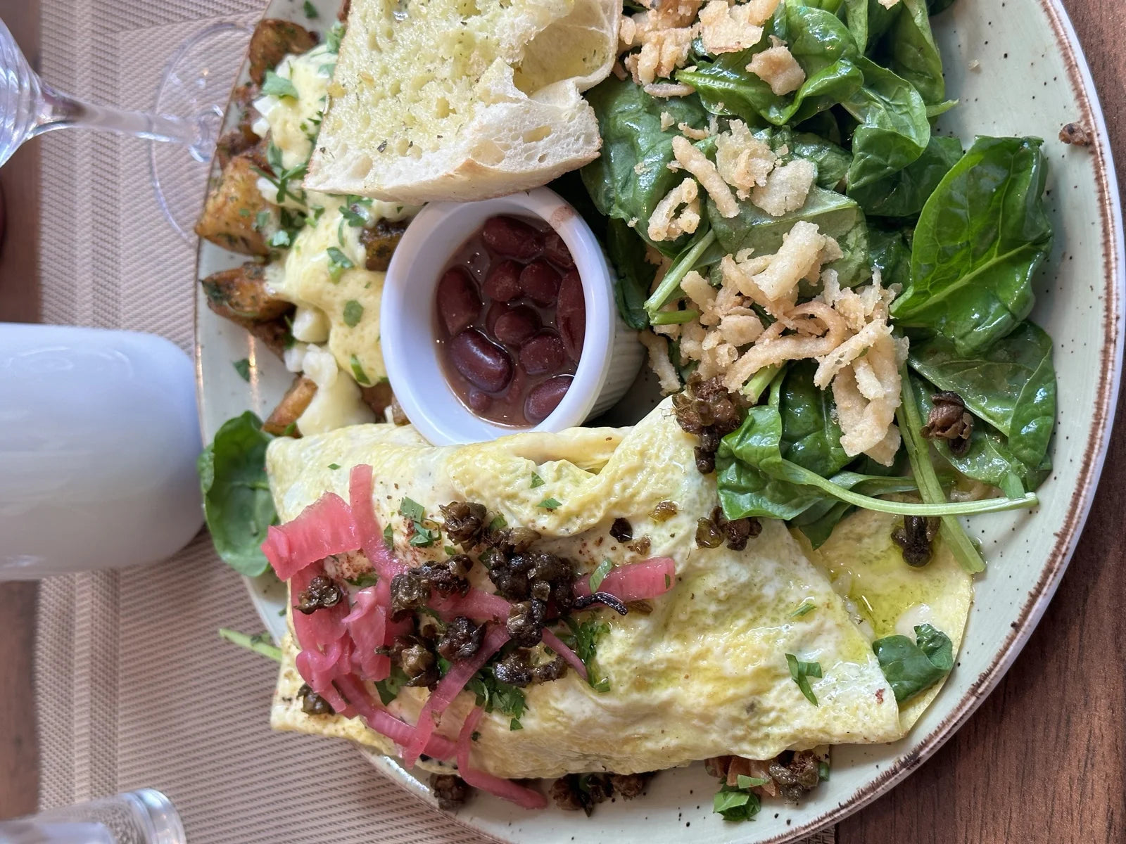 overhead brunch plate: omelette w/ pickled onion + fried capers, spinach salad w/ crisp…