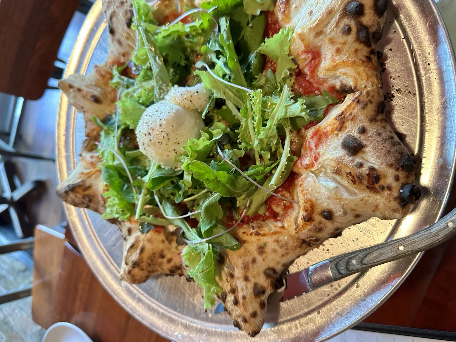 wood-fired pizza on metal tray w/ arugula, burrata, and tomato sauce, dark leopard-spot…