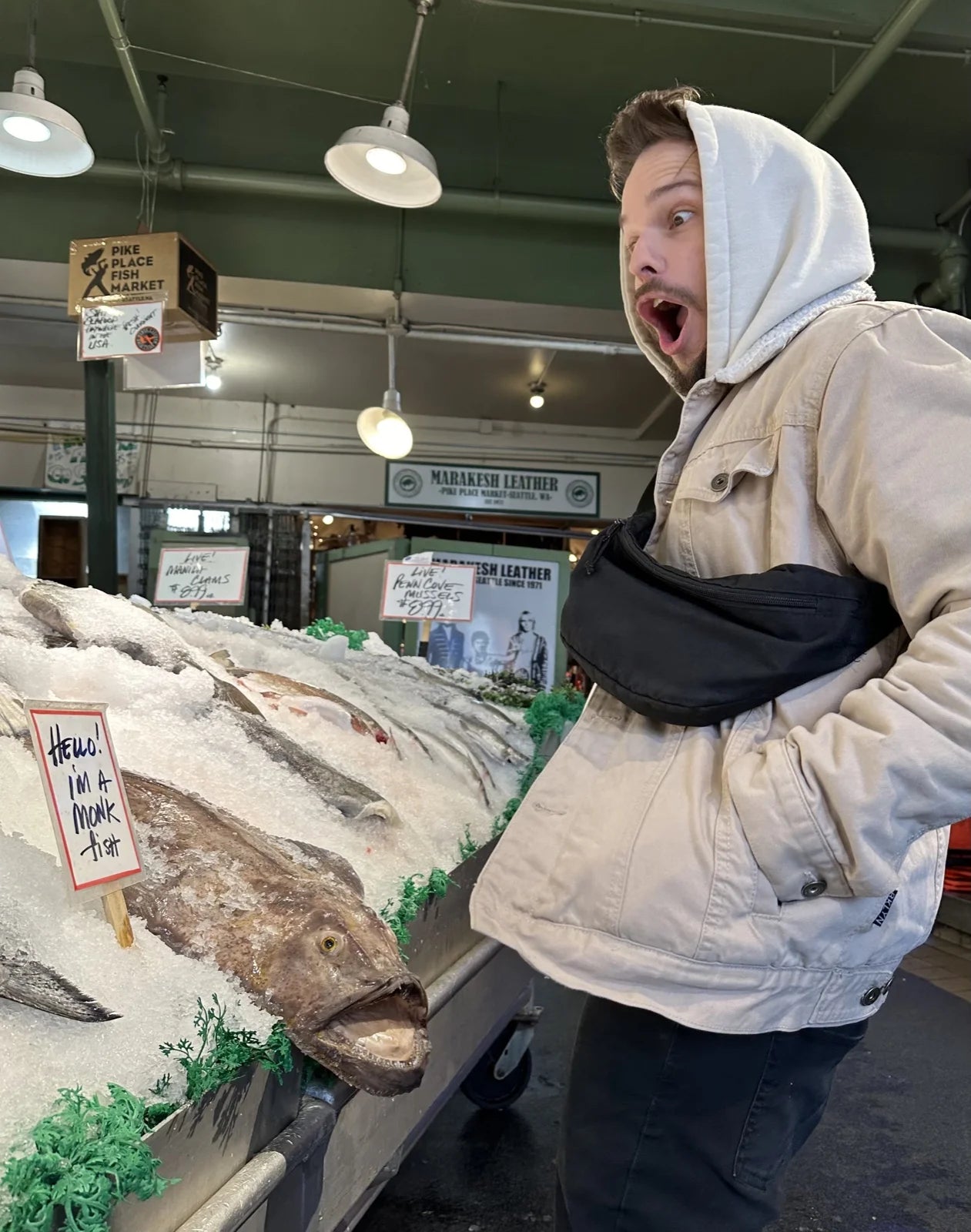 Robby in white hoodie mock-shocked at a monkfish on ice at Pike Place Fish Market (Mara…