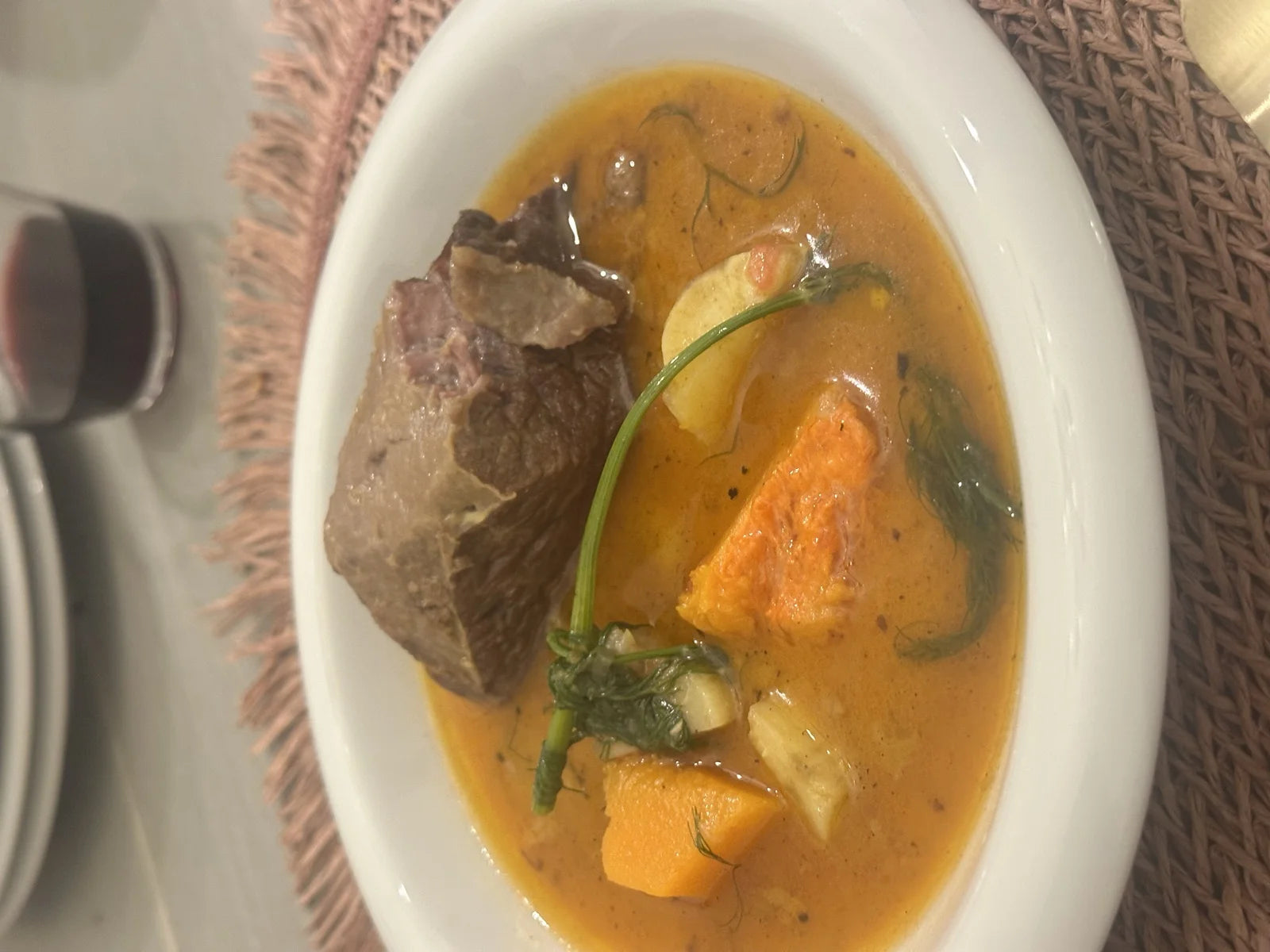 white bowl of braised short rib / oxtail in broth w/ carrots, sweet potato, herbs; glas…