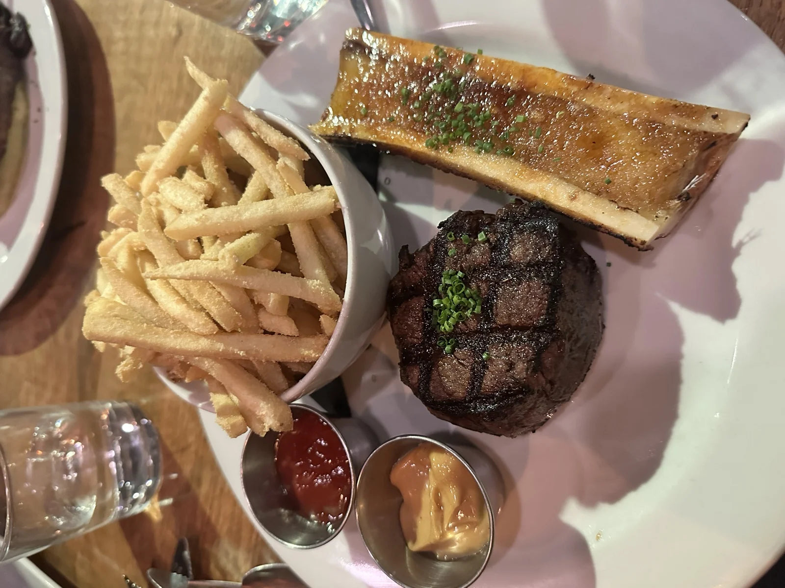 close-up of filet mignon w/ bone marrow scoop + chives on a pink plate, side of shoestr…
