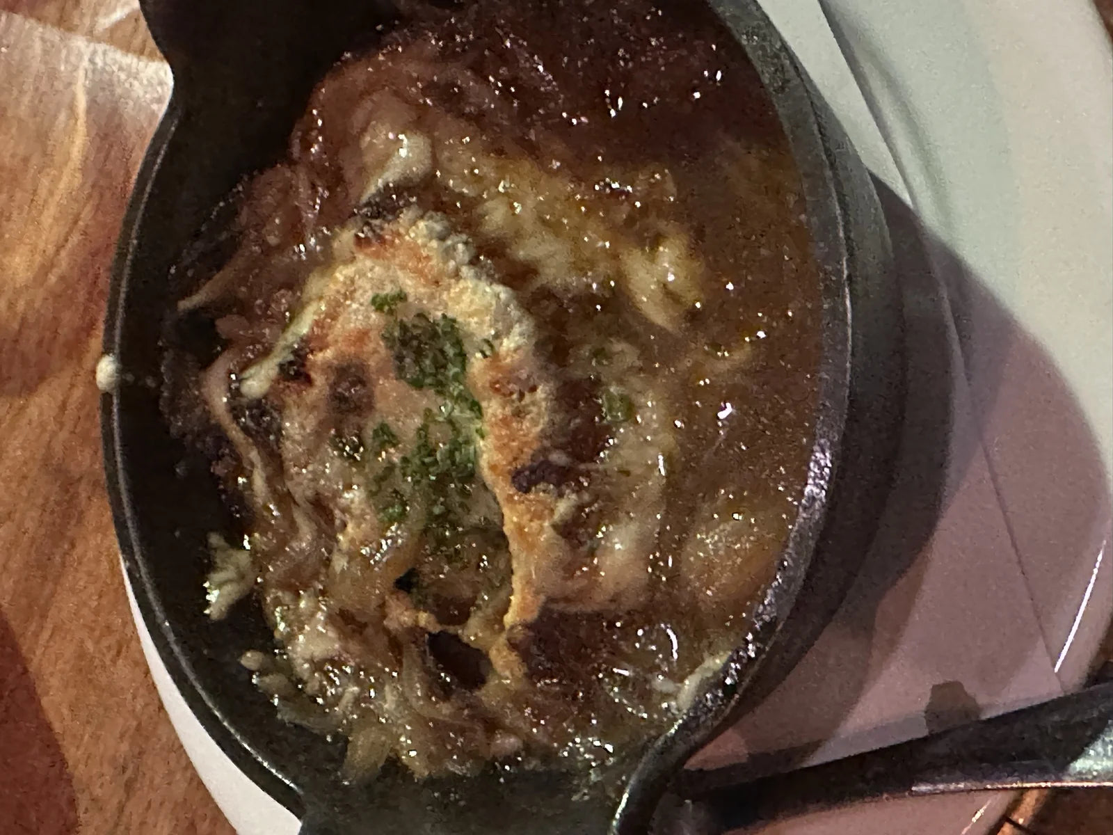 cast-iron crock of French onion soup w/ broiled melty gruyere crust, herbs on top
