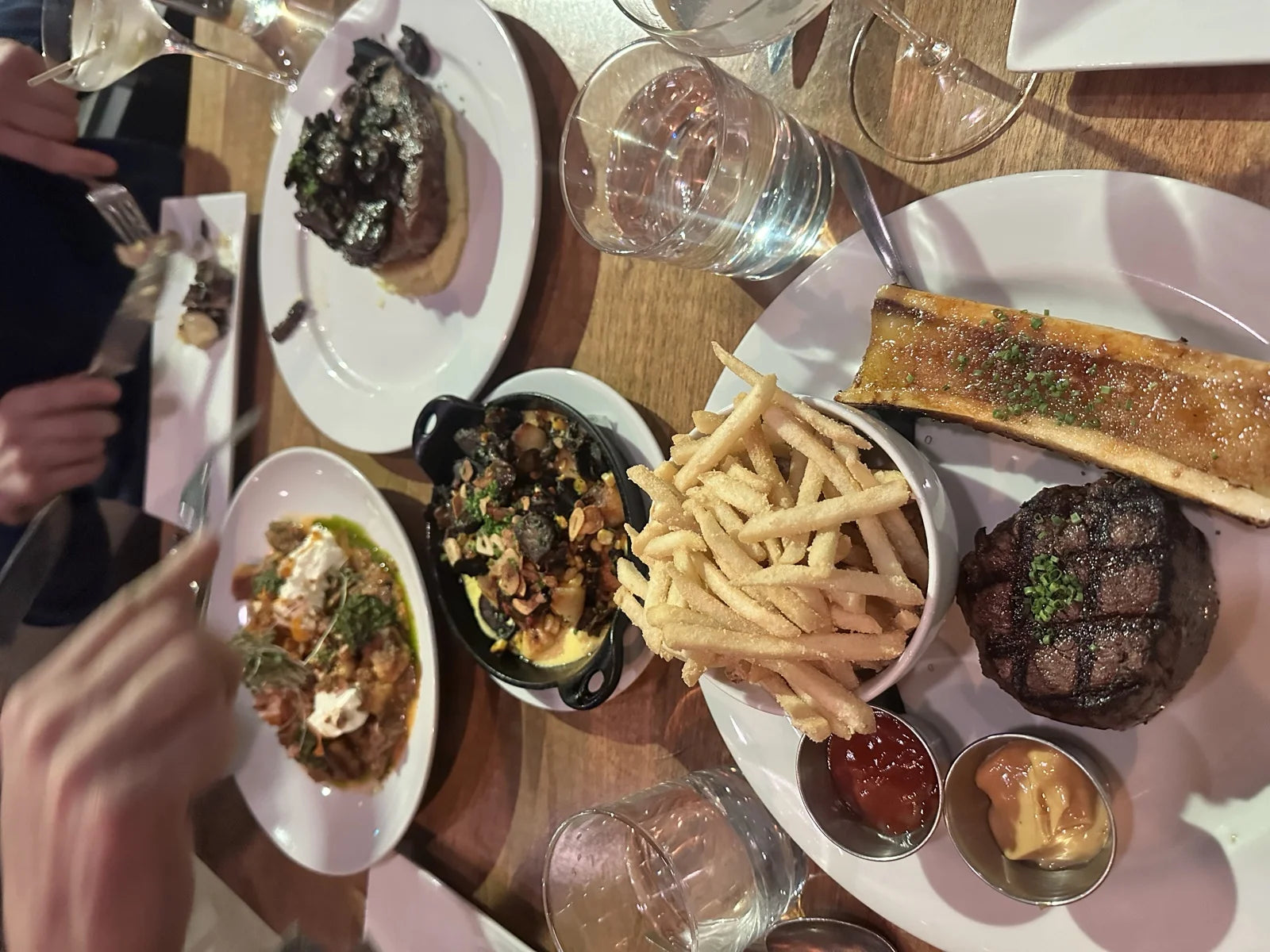 overhead of full steakhouse spread: gyoza, mushroom ragout, fries, filet w/ bone marrow…