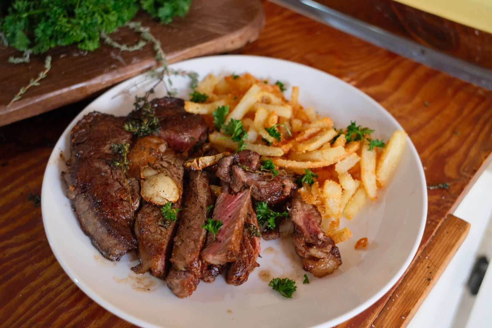 sliced medium-rare ribeye w/ garlic + herbs + shoestring fries + parsley on a white pla…